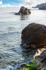 seascape with rock in the water. textured boulder reflecting calm sea surface in morning light. vacation season in summer. sunny weather. fluffy clouds above horizon