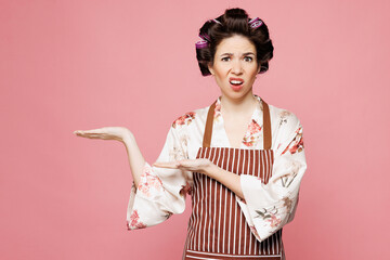 Young shocked indignant sad housewife housekeeper chef cook baker woman wear brown apron point hands aside on area isolated on pastel light pink color background studio portrait. Cooking food concept.