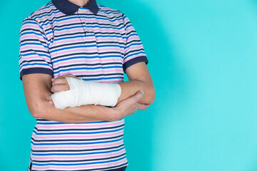 Medical Concepts. Closeup of Body Parts of Caucasian Man in Striped Shirt with Broken Hand In Plaster and Bandaid Isolated on Turquoise
