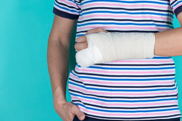 Medical Concepts. Closeup of Caucasian Man Damaged Broken Hand In Plaster and Bandaid Isolated on Turquoise Background.