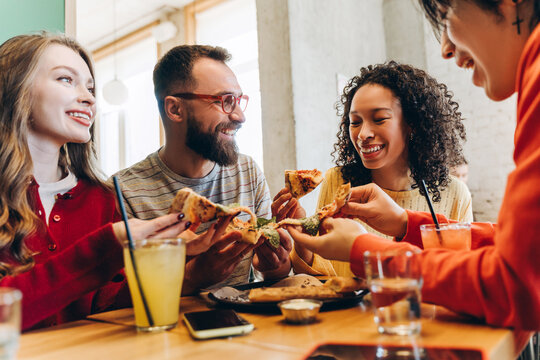Happy friends sharing pizza and drinks at restaurant table