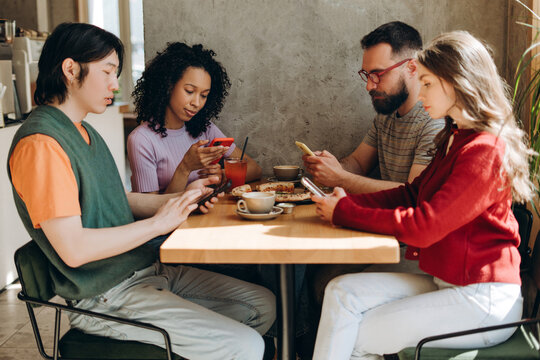 Young people ignoring each other while using smartphones at cafe - Powered by Adobe