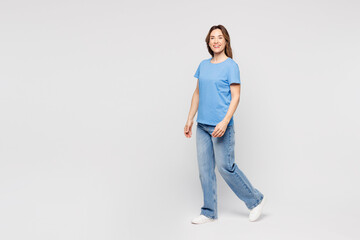 Full body side profile view smiling cheerful happy young woman she wears blue t-shirt casual clothes walk go stroll isolated on plain solid white color background studio portrait. Lifestyle concept.