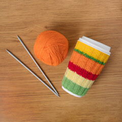 Cup for takeaway coffee with knitted autumn striped cover and knitted wool with knitting needles on...