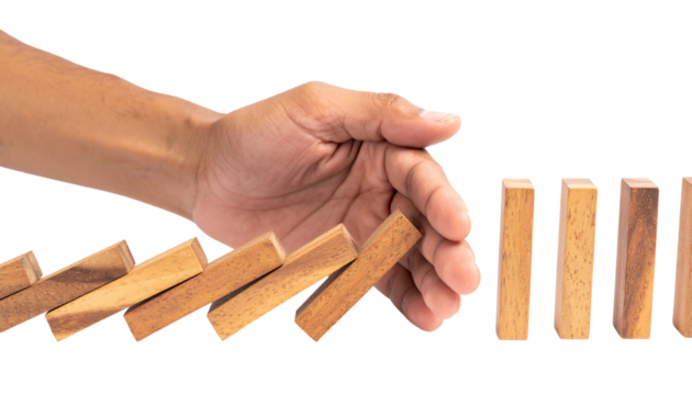 A hand stops falling wooden dominoes from knocking over the remaining standing pieces.