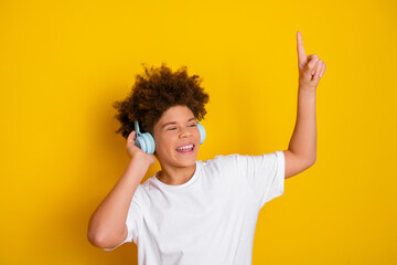 Happy boy wearing headphones and dancing while enjoying music with a gesture on a yellow background