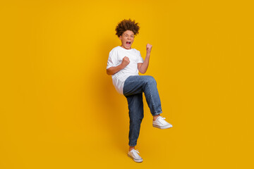 Happy young boy celebrating in casual outfit against bright yellow solid background showing cheerful emotions