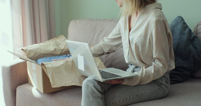 Happy shopaholic female unpacking parcel box at home. Female customer shopper receiving online shop purchase buying clothes unpacking delivery package.