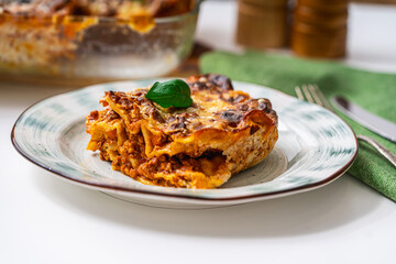 A piece of lasagna according to a traditional Italian recipe on a plate on a light background and in a baking dish. Close-up.