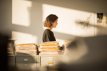 Early afternoon in a spacious office with neutral colors A worker is sorting through a stack of papers, organizing them by category