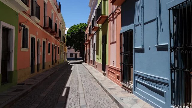 Colorful colonial street with pastel facades and shadows under bright sunlight in a narrow Latin American alley

