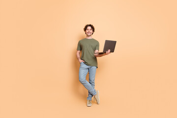 Young man posing casually with a laptop against a beige backdrop, wearing trendy khaki attire
