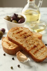 Toasted bread with oil, olives and spices on white marble table, closeup