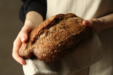Woman with fresh loaf of bread on grey background, closeup