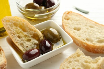 Slices of bread with oil and olives on white wooden table, closeup