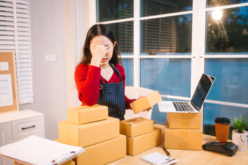 A middle-aged woman, who appears to be Asian, rests her forehead on her hand, looking stressed and...