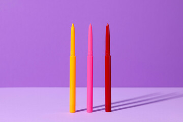Colorful twist up eye pencils on purple background, closeup