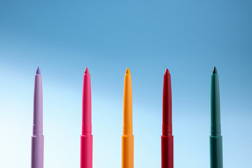 Colorful twist up eye pencils on light blue gradient background, closeup