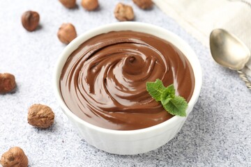 Tasty chocolate spread with mint in bowl and hazelnuts on grey textured table, closeup