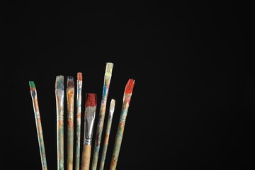 Many dirty paintbrushes on black background, closeup. Space for text
