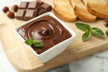Tasty chocolate spread, pieces, toasts, mint and hazelnuts on white marble table, closeup