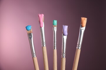Fototapeta premium Many brushes with color paints on pink background, closeup