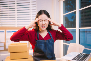 A middle-aged woman, who appears to be Asian, rests her forehead on her hand, looking stressed and...
