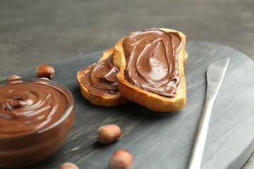 Toasts with tasty chocolate spread and hazelnuts on gray table, closeup
