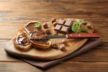 Toasts with tasty chocolate spread, pieces, mint and hazelnuts on wooden table, closeup