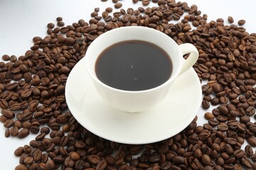 Aromatic coffee in cup and beans on white background, closeup