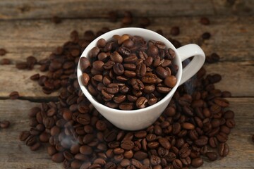 Aromatic coffee beans and cup on wooden table, above view
