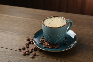 Aromatic coffee in cup and beans on wooden table, closeup. Space for text
