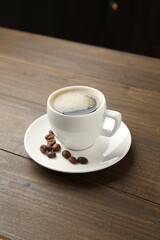 Aromatic coffee in cup and beans on wooden table