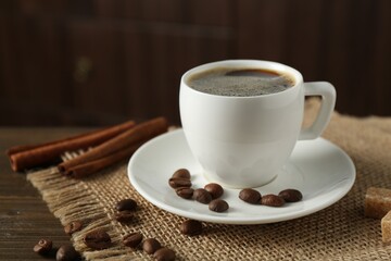 Aromatic coffee in cup, beans, brown sugar and cinnamon on wooden table, closeup