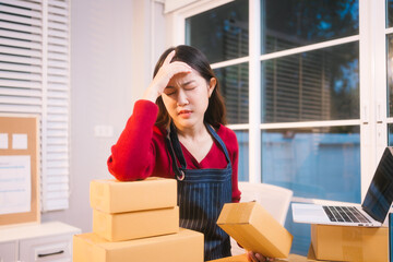A middle-aged woman, who appears to be Asian, rests her forehead on her hand, looking stressed and...