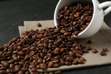 Aromatic coffee beans and overturned cup on black table, closeup