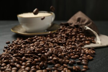 Aromatic coffee beans and hot drink on black table, closeup