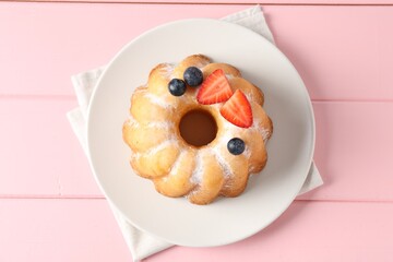 Tasty Bundt cake with powdered sugar and berries on pink wooden table, top view.