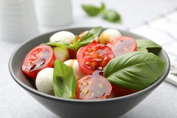 Tasty salad with mozzarella, tomatoes and basil on light table, closeup