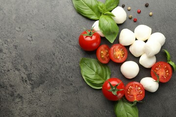 Mozzarella cheese, tomatoes, basil and peppercorns on grey table, flat lay. Space for text