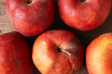 Many rotten red apples on wooden table, closeup