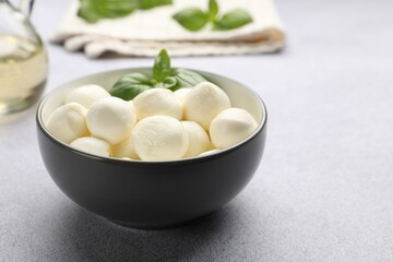 Tasty mozzarella cheese balls and basil on light grey table, closeup. Space for text