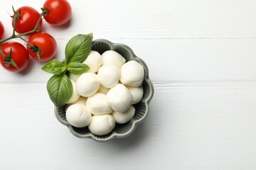 Tasty mozzarella cheese balls, tomatoes and basil on white wooden table, flat lay. Space for text