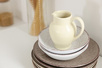 Clean ceramic jug, bowls and plates on white table in kitchen, closeup. Space for text