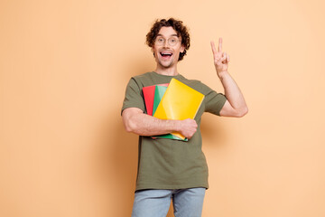Happy young man in casual attire holding notebooks and making a victory sign with an energetic...