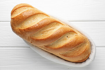 One bread loaf in basket on white wooden table, top view