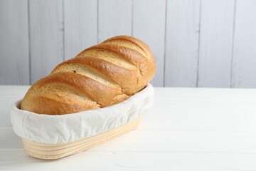One bread loaf in basket on white wooden table, space for text