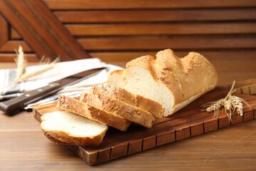 Cut bread loaf, spikelets and knife on wooden table, closeup