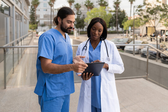 Two diverse multiethnic doctors standing outside a hospital using a tablet discussing patient data