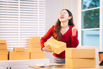 A smiling woman, who appears to be a middle-aged Asian individual, stacks cardboard boxes on a desk...
